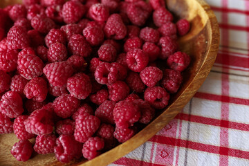 A wooden bowl with ripe raspberries lies on a rustic tablecloth.