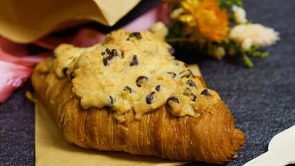Freshly baked crookie croissant topped with a chocolate chip cookie, creating a tempting pastry combination on parchment paper against a dark background