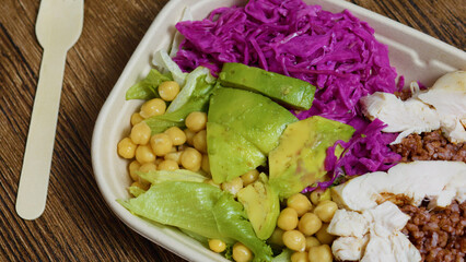 Balanced and nutritious lunch bowl featuring grilled chicken, creamy avocado, protein rich chickpeas, and vibrant red cabbage on a rustic wooden table