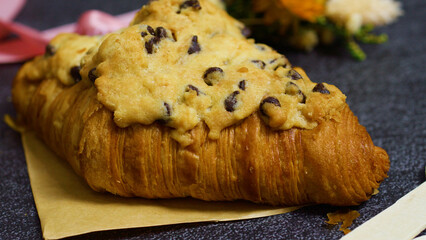 Freshly baked crookie croissant topped with a rich chocolate chip cookie, creating a delightful pastry fusion resting on parchment paper, inviting indulgence with every bite