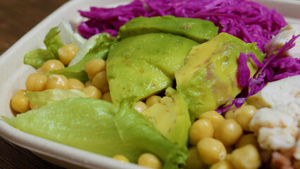 Close up of a vibrant and nutritious vegan lunch bowl featuring sliced avocado, chickpeas, fresh lettuce, red cabbage, and tofu, promoting a healthy and balanced lifestyle