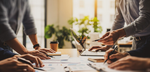 People working at a table with laptop and documents in an office, collaborating on a shared task while analyzing data and organizing files in a productive workspace environment.