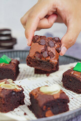 Baked chocolate brownie pieces, with a hand in frame photo concept, levitation and a white wooden background