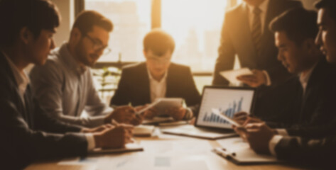 Business people in a meeting around a table with a laptop and documents, actively exchanging ideas and reviewing data during a collaborative discussion in a bright workspace.