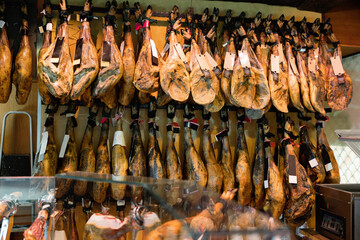 Abundance of dry-cured pig's legs in spanish jamoneria. Lots of preserved pork meat at counter in market.