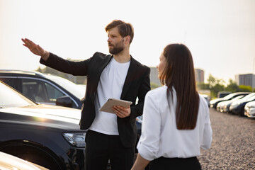 Obraz premium A male car dealer explains a vehicle to a woman at a car dealership.