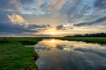 Sunset over calm waters showcasing reflective clouds and lush greenery in a tranquil landscape