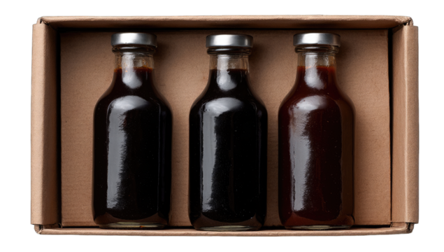 Three small glass bottles of dark sauces in a brown box