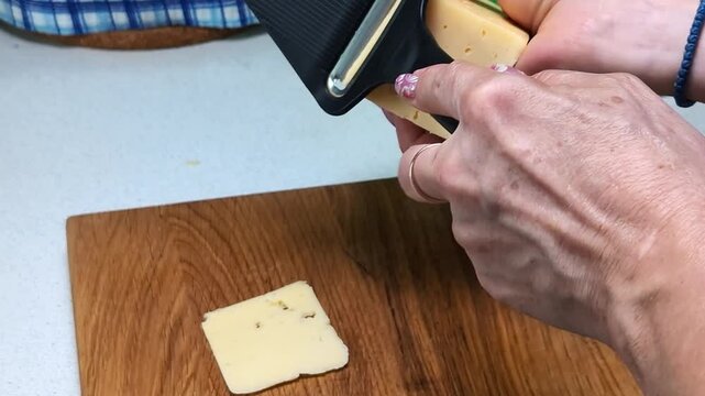 Manually cutting cheese into thin slices with a cheese slicer, close-up