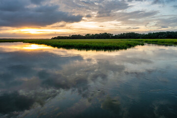 Sunset reflects on tranquil waters of marshland with vibrant sky and lush greenery
