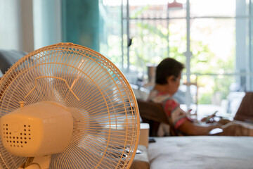 Electric fan blowing air in living room with elderly woman sitting and relaxing in the background at home