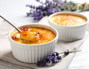 Perfectly caramelized crème brûlée in white ramekins, spoon cracking the sugar crust 