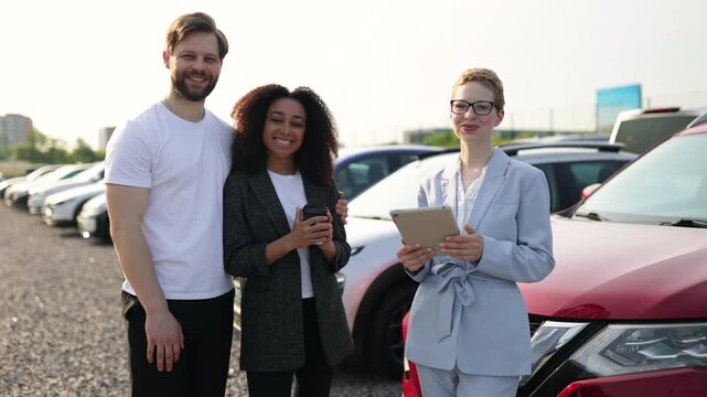 Three people at a car dealership giving a thumbs up in front of a red car, showcasing customer satisfaction.