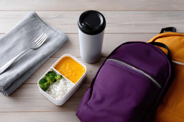 Student backpacks, lunchbox with healthy food and thermos on wooden table