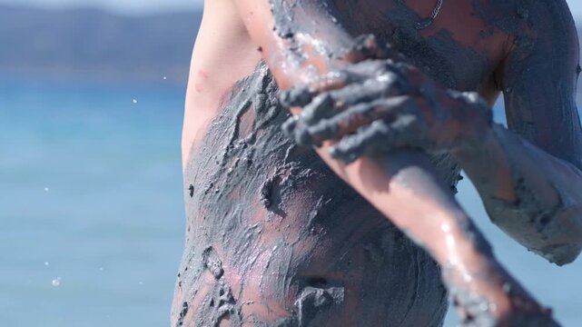 Enjoy the therapeutic effects of healing mud as it is applied to the skin, showcasing its rejuvenating properties against a beautiful beach backdrop.