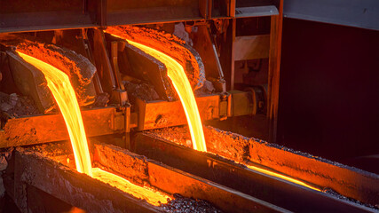 A dynamic industrial scene captures molten metal pouring into molds. The intense glow and high-temperature environment evoke power, heat, and raw material processing.