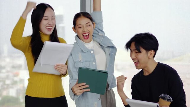 Asian business team professionals in an office setting joyfully celebrates their recent achievement. Their smiles and raised fists embody motivation and unity in success, group achievement