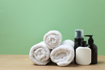 White towel and bathroom toiletries on wooden table with green background
