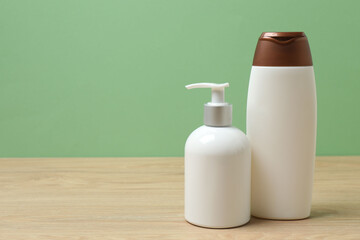 White bottles of toiletries on a wooden table with a green background