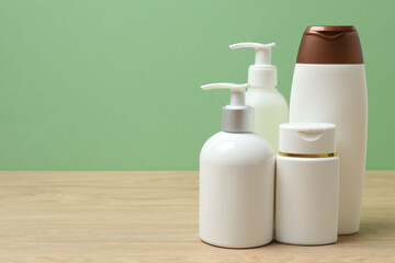 White bottles of toiletries on a wooden table with a green background
