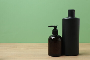 Black bottles of toiletries on a wooden table with a green background
