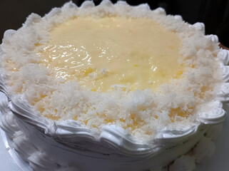 Top view of a coconut cream cake topped with shredded coconut and glossy custard, surrounded by piped whipped cream.