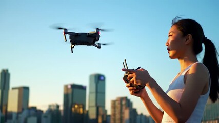 Woman operating drone remote over cityscape at sunrise