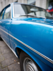 Blue classic car parked on a city street, close-up side view.