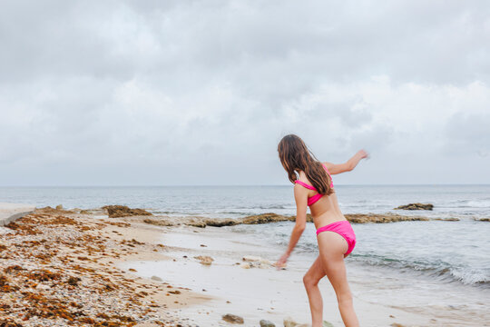 Girl walks alone on empty beach in pink bikini