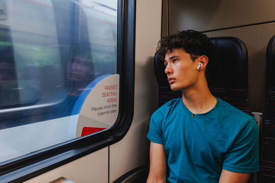 A teen boy looks window at passing train listening to music