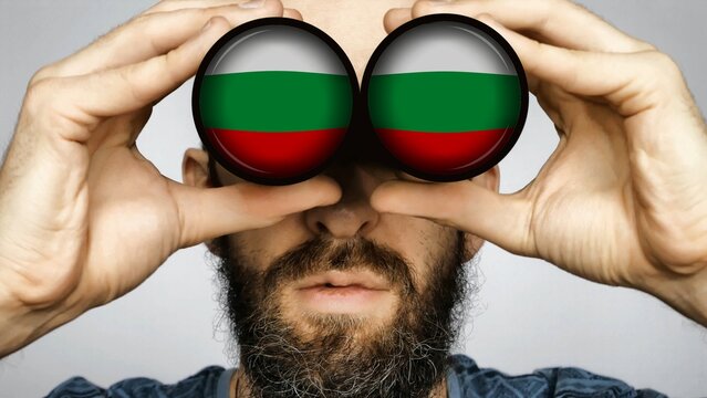 The Bulgarian flag is reflected in the lenses of binoculars through which a bearded man looks