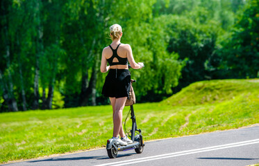 Fototapeta premium Girl rides an electric scooter in the summer Park 
