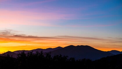 Fototapeta premium Mountain range silhouette under a vibrant sunset sky with orange and purple hues