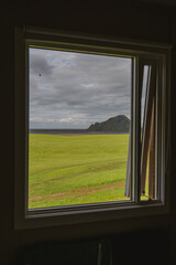 Fototapeta premium View Through a Window of Green Field, Rocky Hill, and Coastline