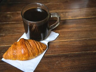Breakfast menu. Croissant and a cup of black coffee on a wooden table.