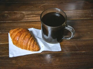 Breakfast menu. Croissant and a cup of black coffee on a wooden table.
