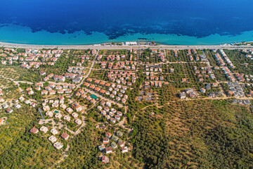 Drone capturing a residential area along the coast, showcasing houses, roads, trees, and the beautiful turquoise waters of mediterranean sea