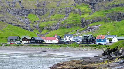 Colorful houses along the rugged coast of Faroe Islands under dramatic cliffs