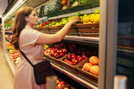 Young woman customer takes out a green apple from the shelf in the grocery store