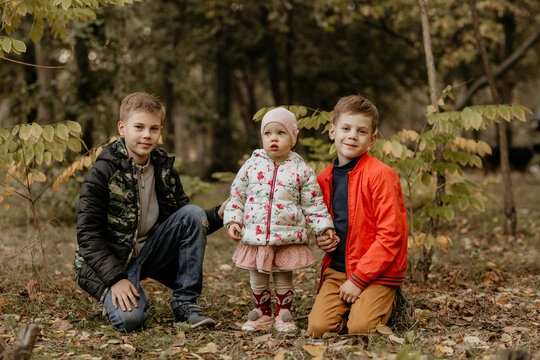 Three siblings standing in autumn forest, two brothers with toddler sister outdoors among trees and colorful fallen leaves, autumn concept, high quality photo