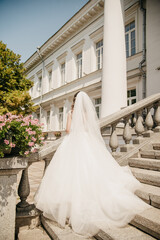 bride in a white dress with a long train stands on the steps of a medieval manor