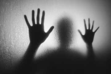 Silhouette of halloween zombie or ghost hands reaching out behind frosted glass