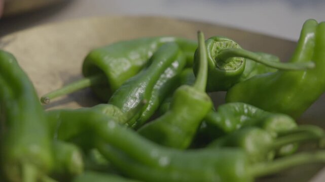 A bunch of green peppers are on a plate. The peppers are long and skinny, and they are all green in color