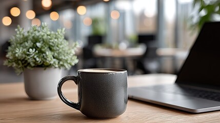 Modern Office Desktop: Dark Gray Coffee Cup with Laptop, Green Potted Plant and Blurred Office Area
