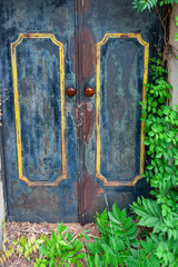 An old, weathered blue door with peeling paint and rust, featuring ornate yellow trim and two round, reddish-brown doorknobs