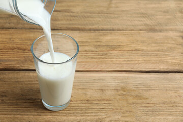 Closeup of pouring fresh milk from jug into glass at wooden table  