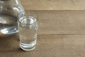 Close up of glass of water with jug at wooden table, closeup. Drinking clear water in the morning for health