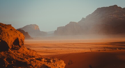 Expansive flat desert landscape in Wadi Rum, Jordan, with distant mountains on the horizon and a large rock formation in the foreground on the left side of the frame.