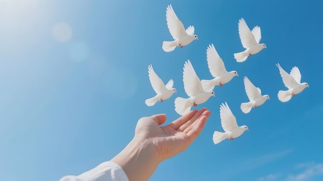 Hand releasing white doves into a clear blue sky, symbolizing peace and freedom. - Powered by Adobe