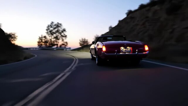 Classic red convertible car driving on a road at dusk